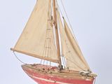 wooden model of a sailboat with a red hull and tan sails