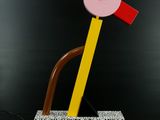 une sculpture en bois représentant un objet rose et jaune posé sur une surface noire