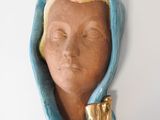 une sculpture en céramique représentant la tête d'une femme coiffée d'une capuche bleue