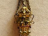 a small gold vase hanging from a chain on a wall