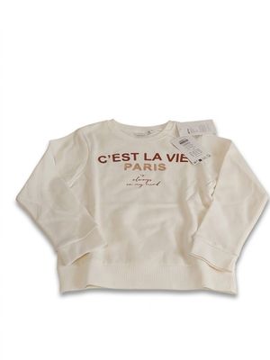 Le pull est blanc et comporte une inscription en rouge.