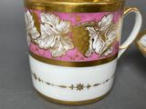 a coffee cup with a gold rim and a pink background