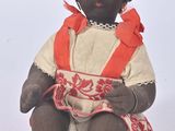 une poupée noire assise sur une surface blanche, vêtue d'une robe rouge et blanche