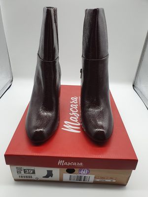 des bottines en cuir noir posées sur une boîte rouge, elle-même posée sur une surface blanche