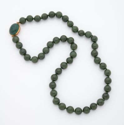 un gros plan d'un collier de perles vertes posé sur une surface blanche
