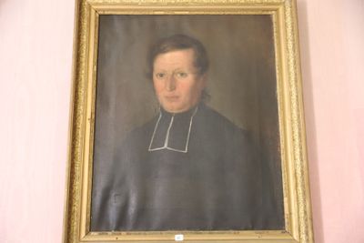 portrait d'un homme en habits sacerdotaux, dans un cadre doré, accroché à un mur rose