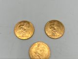On voit trois pièces d'or sur une surface blanche