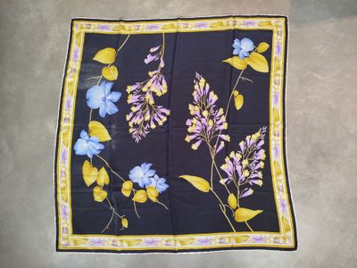des fleurs violettes et bleues sur un foulard carré noir bordé de jaune