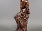 a bronze statue of a man sitting on a rock with his hands on his knees