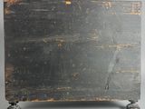 an old black wooden box with wheels on a gray surface