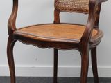 une photo d'une chaise en bois avec une assise en osier, posée sur un sol recouvert de moquette