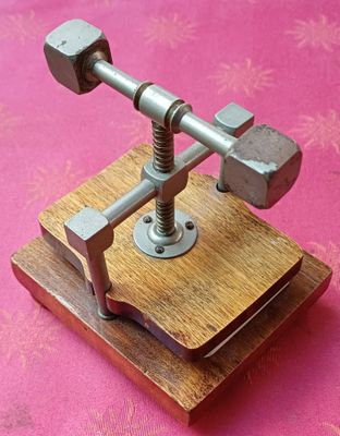 un petit objet métallique posé sur un socle en bois, sur une surface rose
