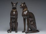two bronze statues of cats sitting next to each other on a gray surface