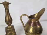 a gold pitcher next to a brass clock on a table