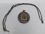 a silver necklace with a coin on it sitting on a white surface
