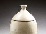 un vase blanc muni d'un couvercle, posé sur une table
