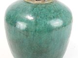 un vase vert posé sur une surface blanche