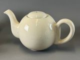 a white tea pot sitting next to a tea cup