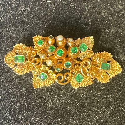 a close up of a gold brooch with green and white stones