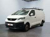La camionnette blanche est garée dans une grande pièce équipée d'une galerie de toit noire.