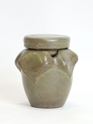 a small green jar with a lid on a white surface