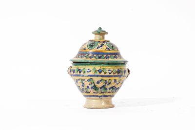 un petit vase muni d'un couvercle, posé sur une surface blanche