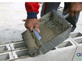 cement being poured into a concrete block with a hand holding a hammer