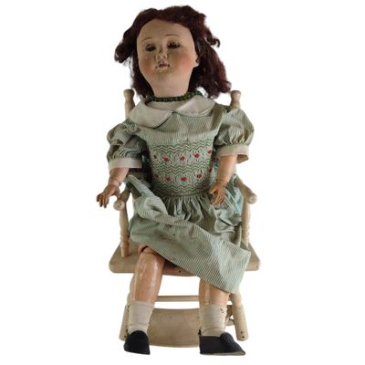 une poupée assise sur une chaise en bois, vêtue d'une robe verte