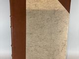 un vieux livre à la couverture marron posé sur une table blanche