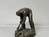 statue en bronze représentant un homme penché pour ramasser quelque chose par terre