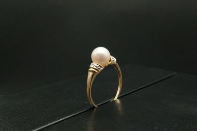 une image représentant une bague ornée d'une perle et de diamants posée sur un fond noir