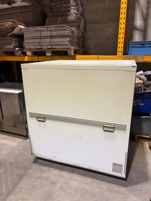 un réfrigérateur blanc posé dans un entrepôt à côté d'une pile de cartons