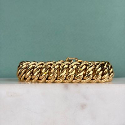 un gros plan d'un bracelet en or posé sur une surface en marbre
