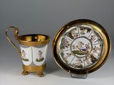 an antique cup and saucer sitting next to a plate with a clock on it