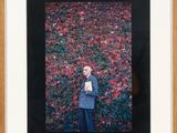framed photograph of a man standing in front of a wall of flowers