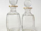 pair of clear glass bottles with gold rims on a white surface
