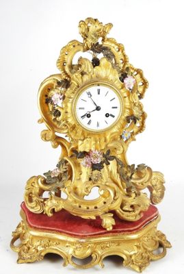a gold clock sitting on a red cushion on a white surface