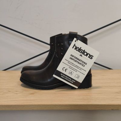 une botte noire avec une étiquette, posée sur une étagère en bois