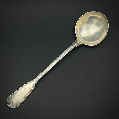 une cuillère ancienne en argent dont le manche repose sur une surface noire