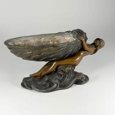 bronze sculpture of a woman holding a shell on a rock