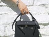 someone is holding a black handbag in front of a white brick wall