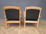 two wooden chairs with black leather seats sitting on a parquet floor