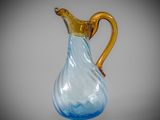 a blue glass pitcher with a gold handle on a gray background