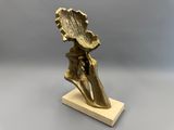 une sculpture en bronze représentant une main tenant une feuille, posée sur un socle en bois