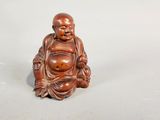a small wooden statue of a smiling buddha sitting on a white surface