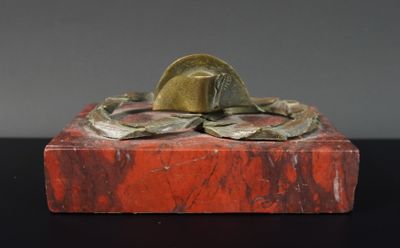 statue d'un homme coiffé d'un chapeau, posée sur un bloc de marbre rouge