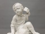 une statue blanche représentant un bébé assis sur un rocher