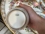 a person holding a cup and saucer in front of a plate