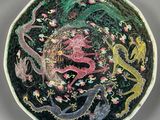 une assiette noire ornée d'un motif représentant un dragon et des fleurs