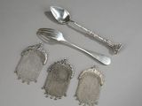 quatre cuillères en argent, une fourchette et un repose-cuillère posés sur une table